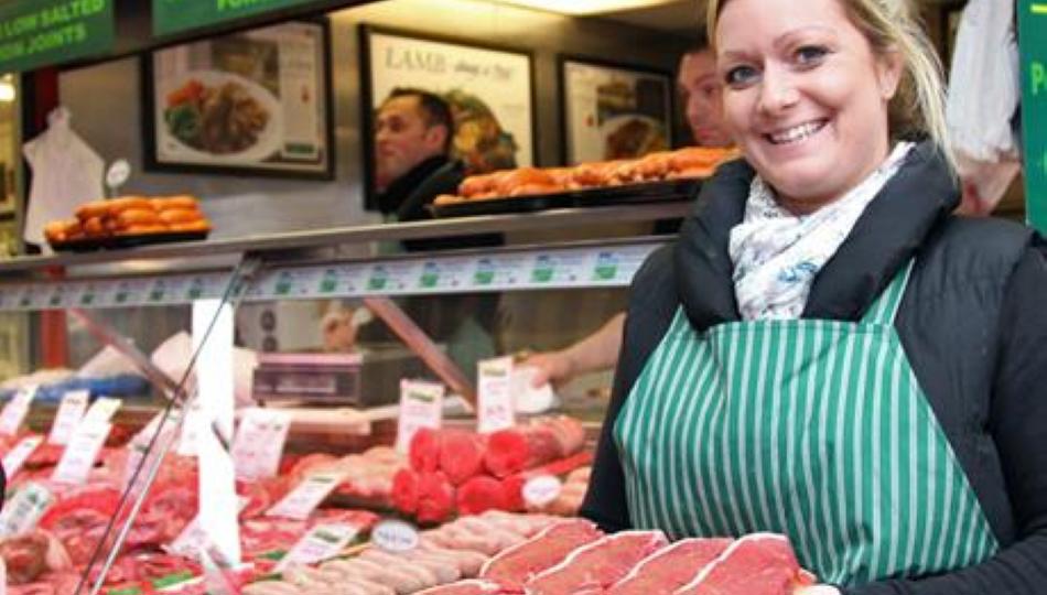 A lady stood next to the meat counter holding a tray of steaks